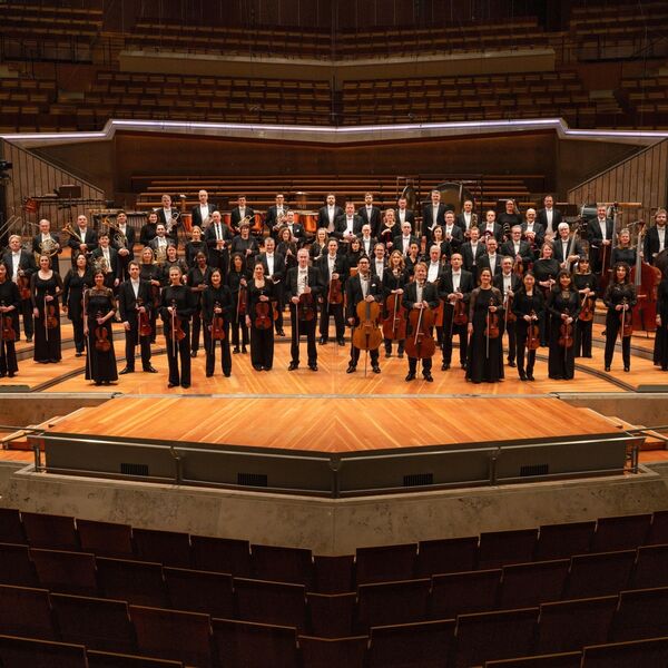 Orchester steht auf einer Bühne vor Publikum
