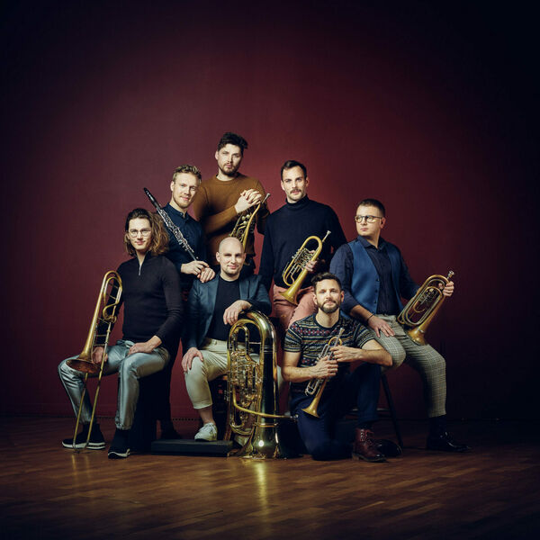 7 Musiker mit Blasinstrumenten vor rotem Hintergrund